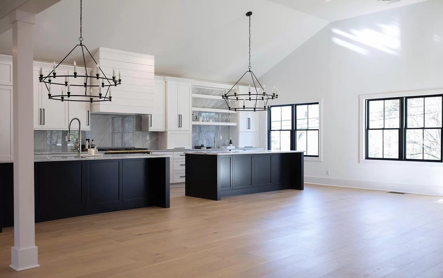 Bright open kitchen with black island cabinets, white walls, large windows, and hardwood floors