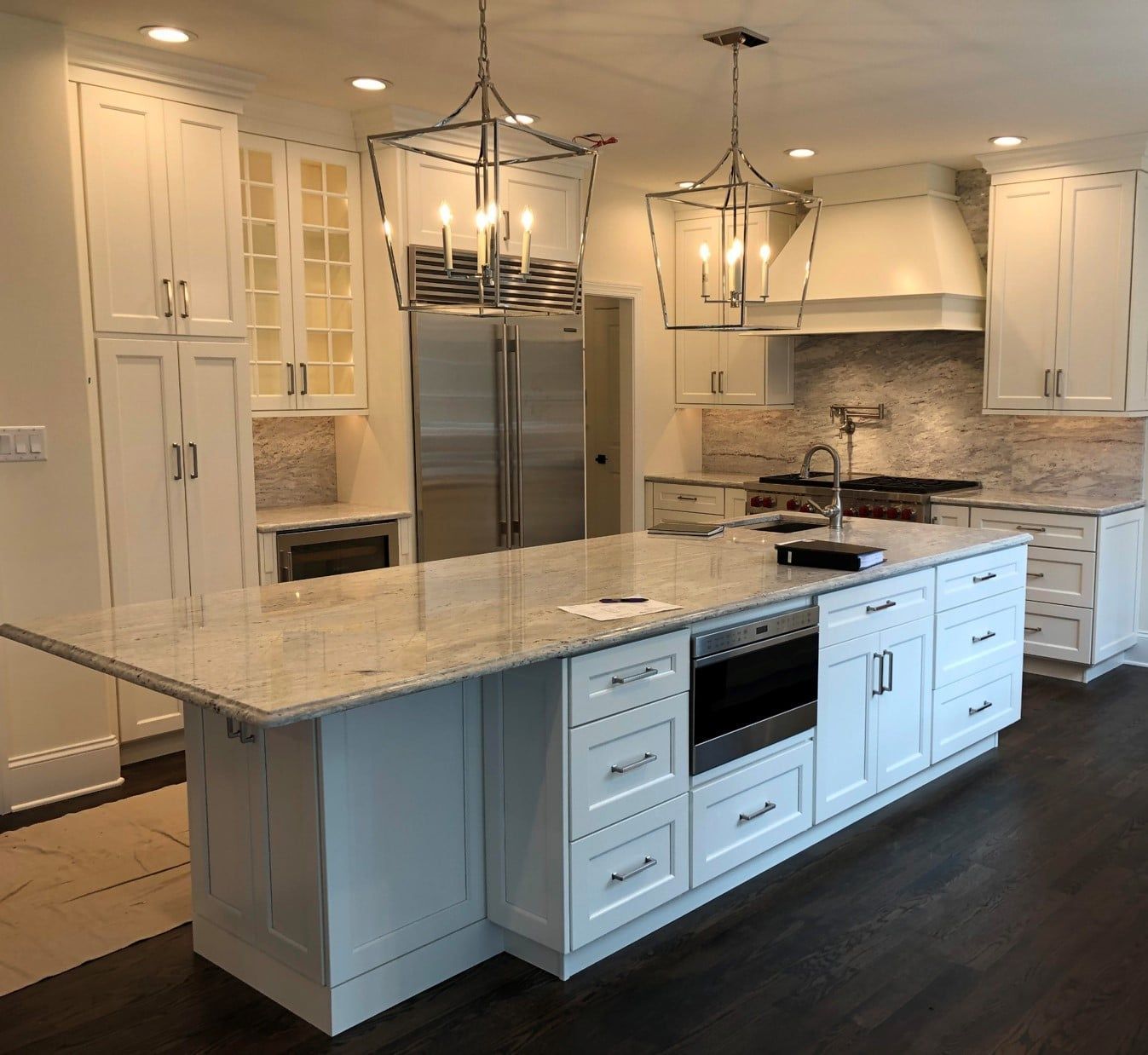 Bright white kitchen with marble island, stainless steel fridge, and hanging pendant lights