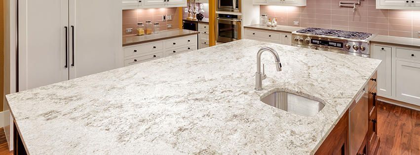 Modern kitchen with a large white marble island and built-in sink, stainless steel appliances, and wood cabinets
