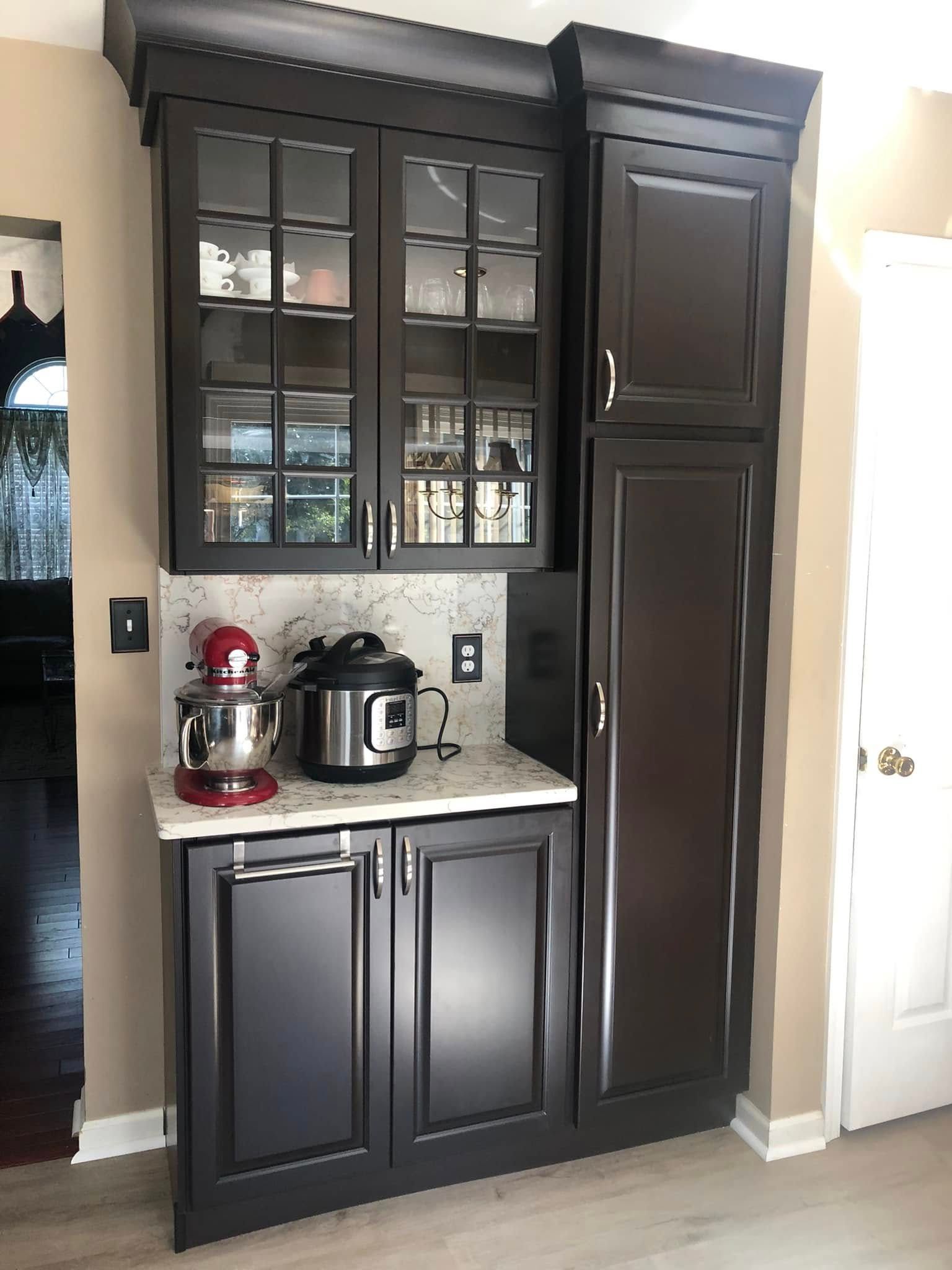 Dark kitchen cabinet with glass doors and countertop appliances, including a red stand mixer and a pressure cooker.