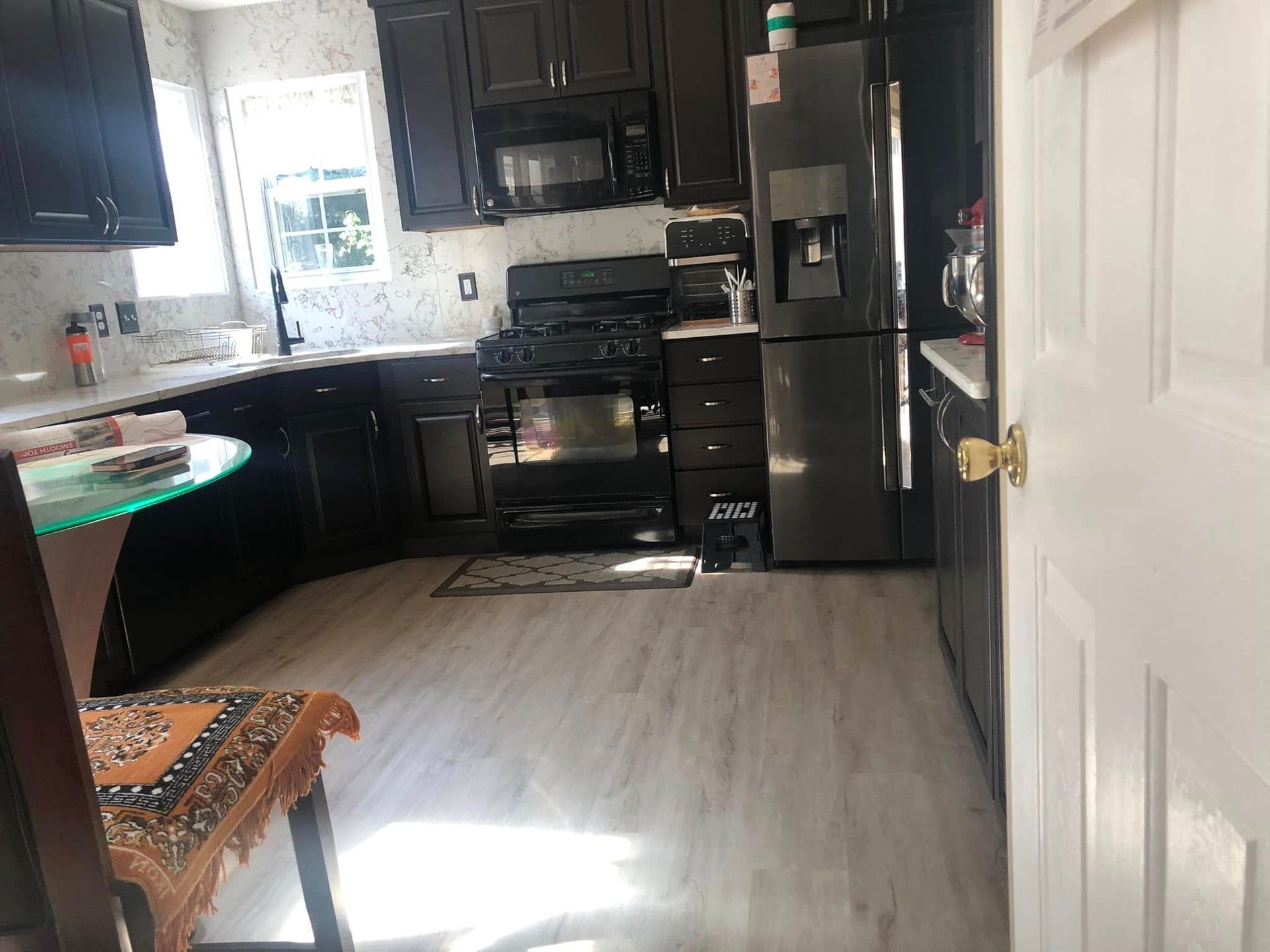 Modern kitchen with dark cabinets, stainless appliances, and a bright window over light wood flooring