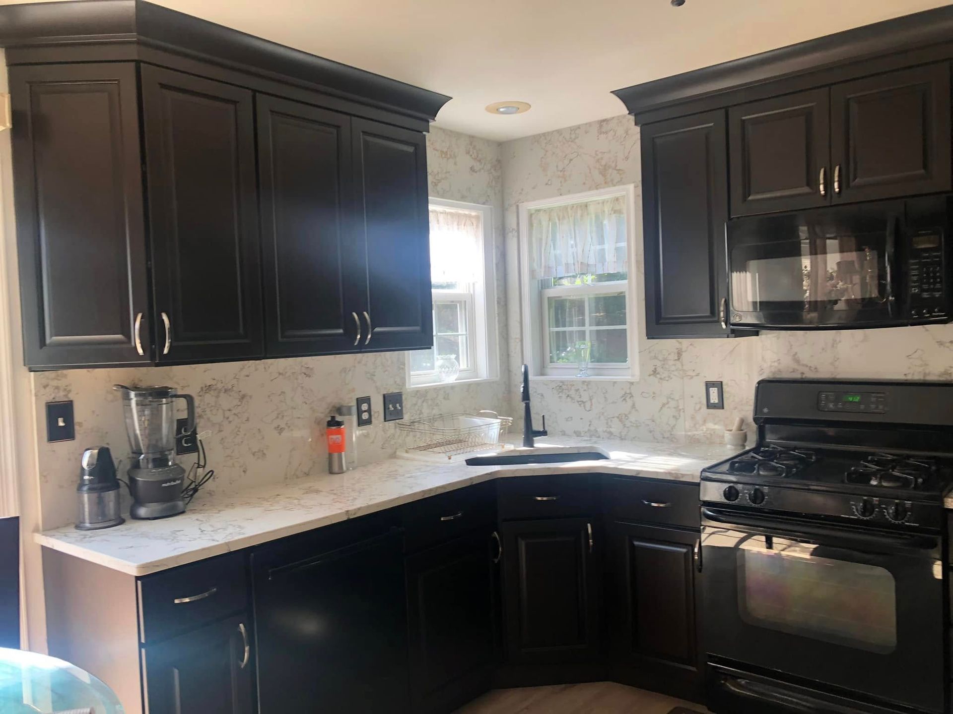 Modern kitchen with dark cabinets, light countertops, window, and black gas stove.