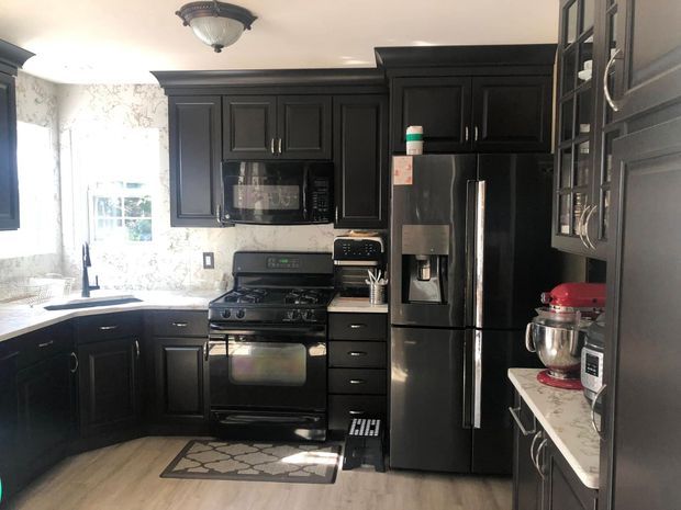 Black kitchen with stainless-steel appliances, dark cabinets, and a window over the sink.