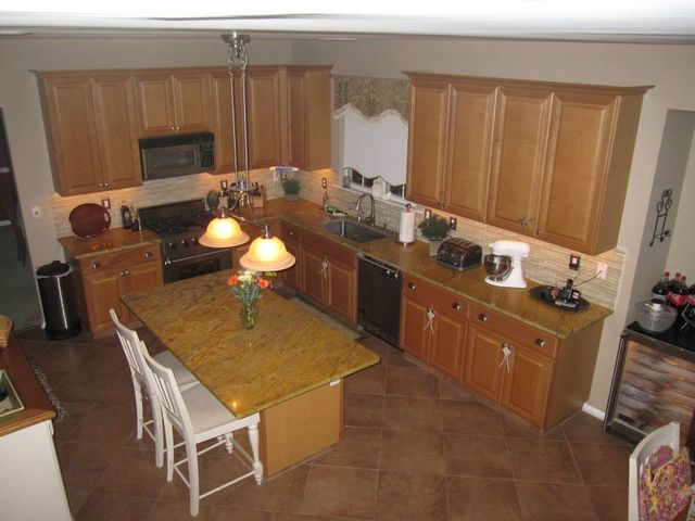 Kitchen with wooden cabinets, tiled floor, island, and pendant lights, viewed from above.