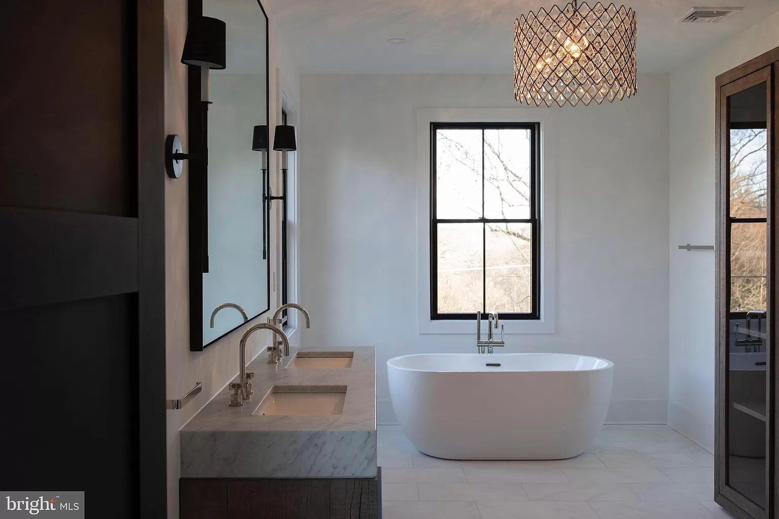 Modern white bathroom with freestanding tub, double vanity, and black-framed window lighting