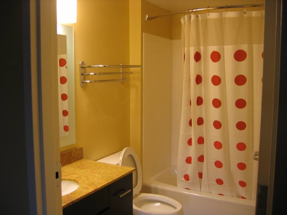 Small bathroom with toilet, sink, mirror, and white shower curtain with red polka dots.