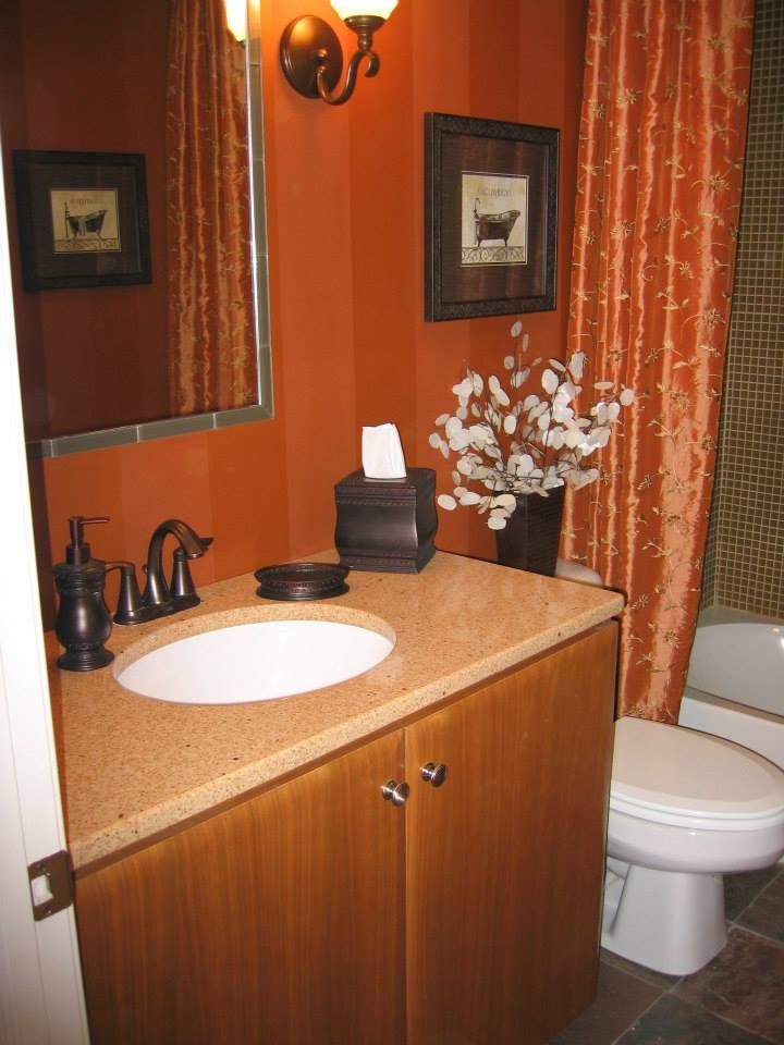Small bathroom with wood vanity, white sink, toilet, mirror, and orange patterned shower curtain.
