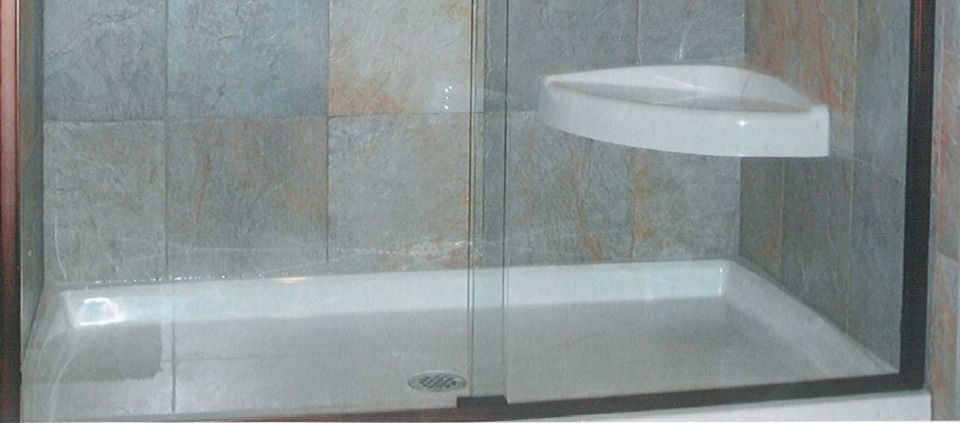 Glass shower stall with white tiled walls and floor, and a wall-mounted shelf inside