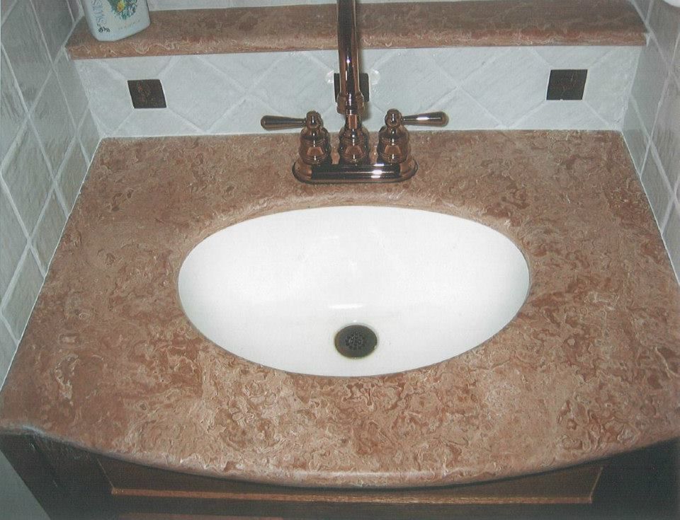 Bathroom vanity with white oval sink, brown countertop, and bronze faucet against tiled wall