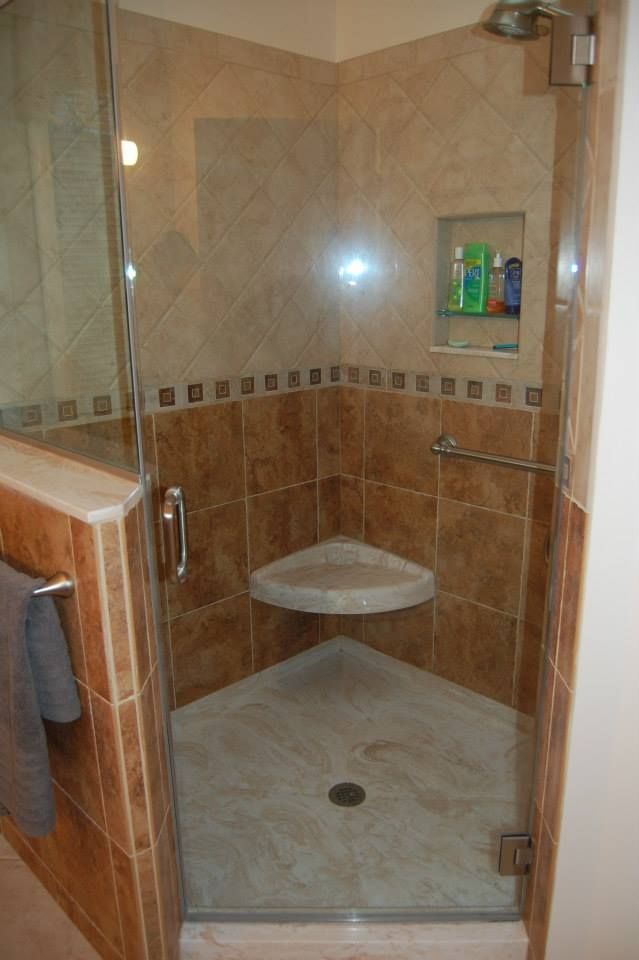 Walk-in shower with beige tile, glass door, built-in corner seat, and handheld shower