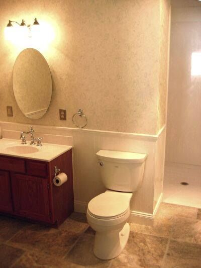 Bathroom with vanity, oval mirror, wall light, and toilet beside a shower stall.