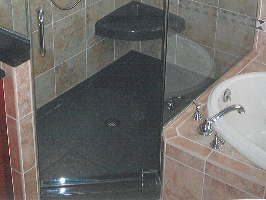 Glass-enclosed corner shower with dark tiled floor and adjacent bathtub sink area