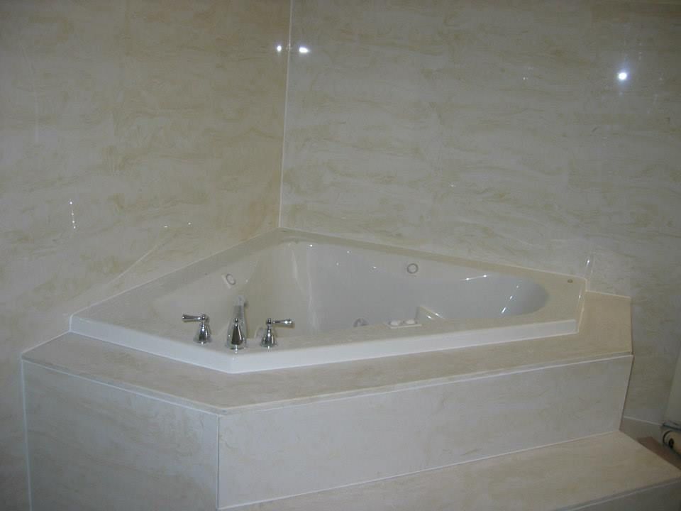 Corner whirlpool bathtub with beige tile surround and chrome fixtures in a bathroom
