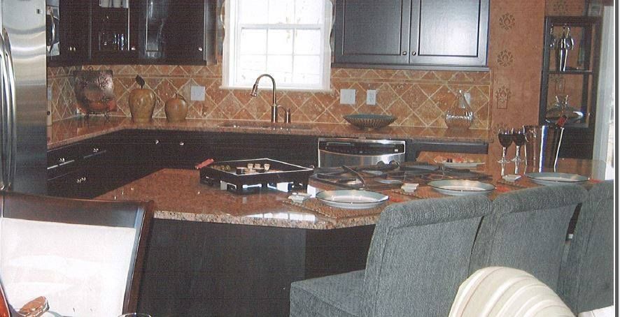 Kitchen with granite island, dark cabinets, window over sink, and upholstered chairs at the counter