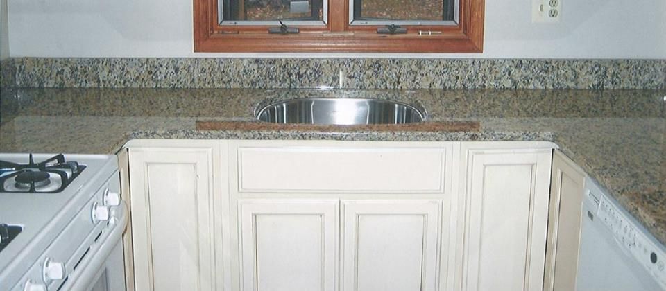 Kitchen sink area with white cabinets, granite countertops, and a window above the sink.