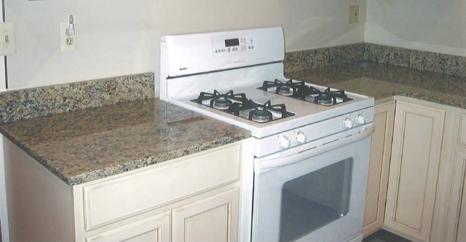 Kitchen corner with white gas stove beside speckled granite countertops and cream cabinets.
