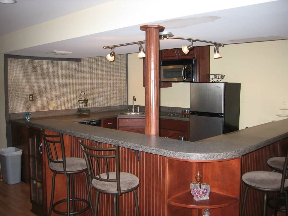 Home bar with granite counter, stools, refrigerator, and tiled backsplash in a basement room