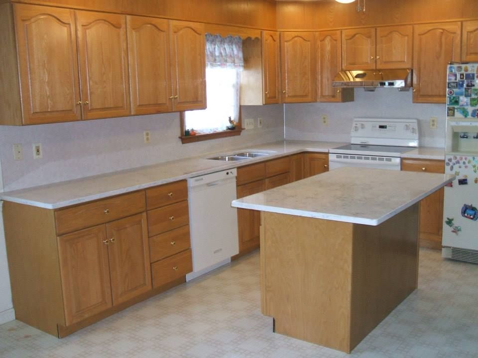 Empty kitchen with oak cabinets, white counters, and a central island under a window