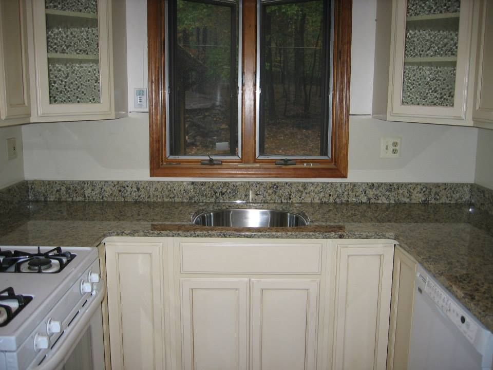 Small kitchen with granite counters, sink under window, and white cabinets beside a gas stove.