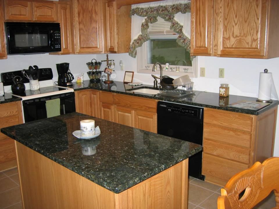 Modern kitchen with wood cabinets, black appliances, granite island, and a window over the sink.