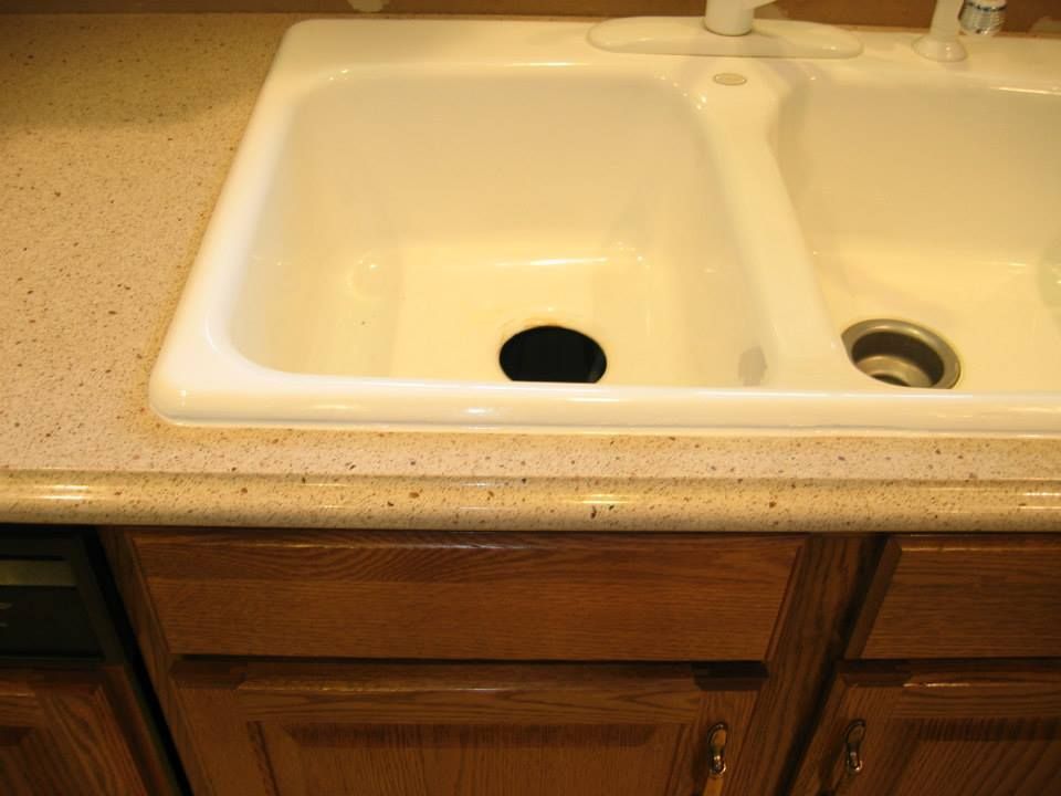 Kitchen sink with black drain cover and wooden cabinet below a speckled countertop