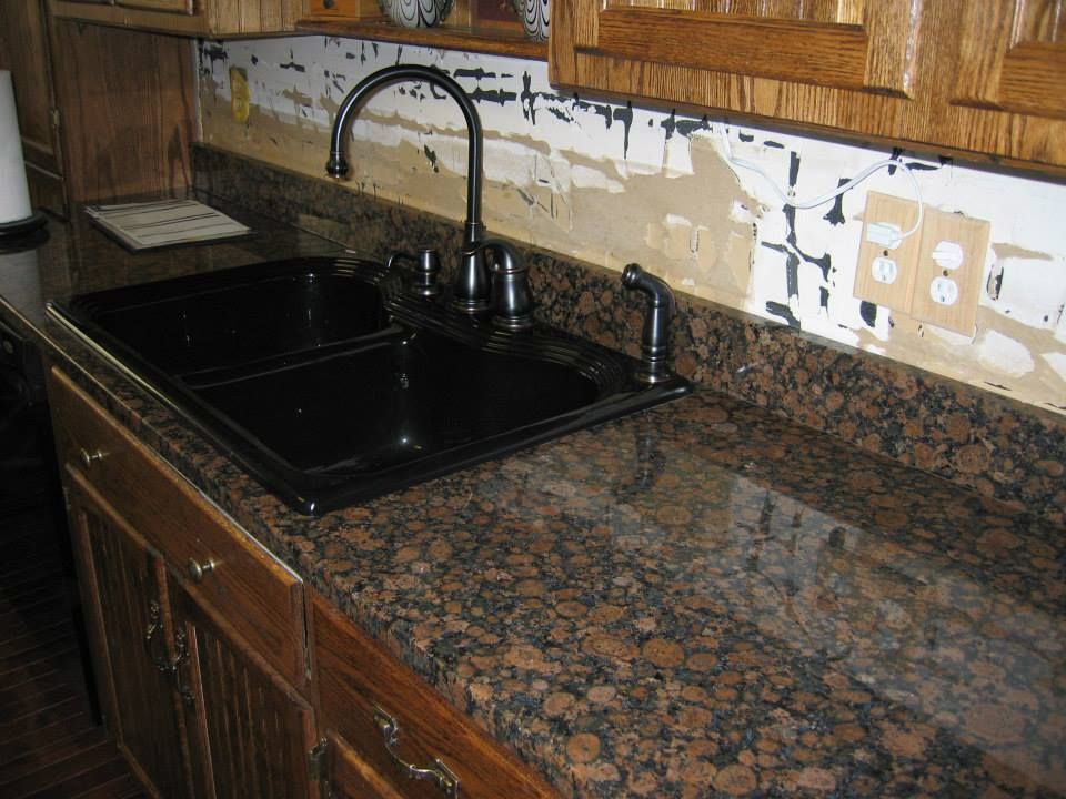 Kitchen countertop with black sink and faucet, brown granite surface, and unfinished backsplash area