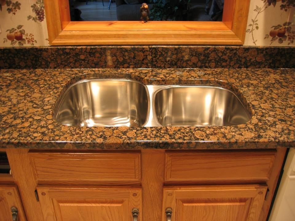 Double-basin stainless steel kitchen sink with granite countertop and wooden cabinets