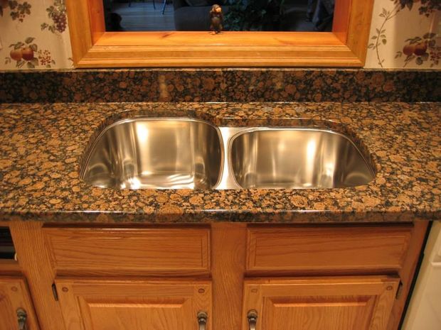 Double stainless steel sink set into speckled granite countertop with wood cabinets beneath