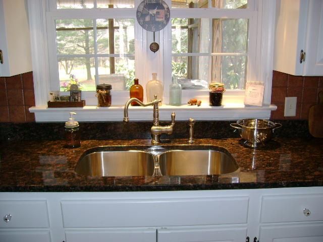 Kitchen sink below a bright window, with dark granite counters and white cabinets