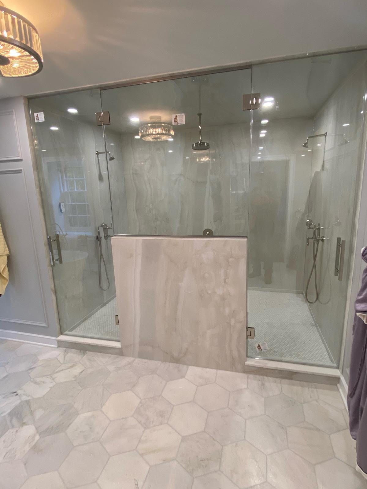 Modern glass shower enclosure with marble-look tile and hexagon floor tiles in a bathroom