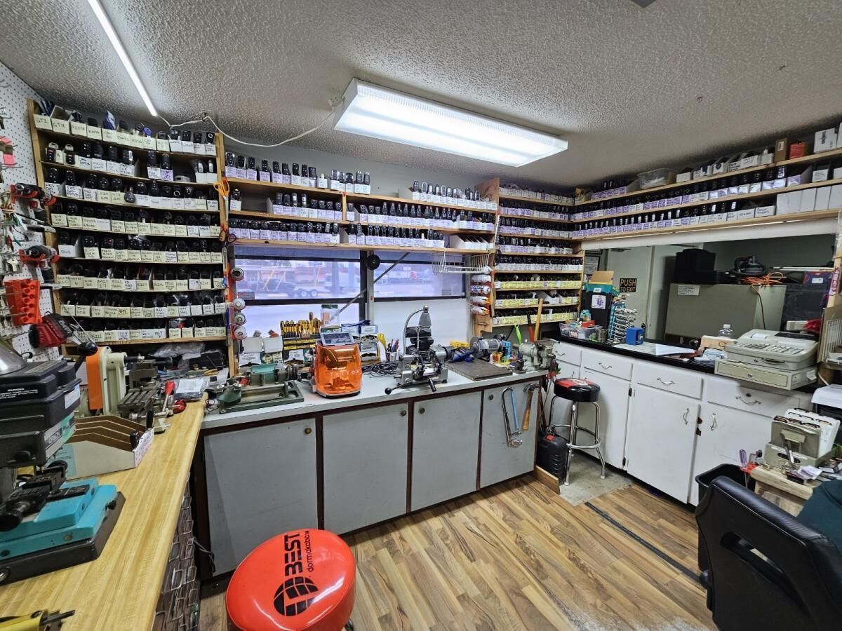 Workshop interior with shelves of parts, workbenches, and tools; a red stool sits in the foreground.
