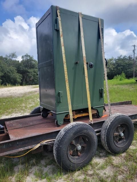A green safe strapped to a trailer, outdoors on a sunny day.