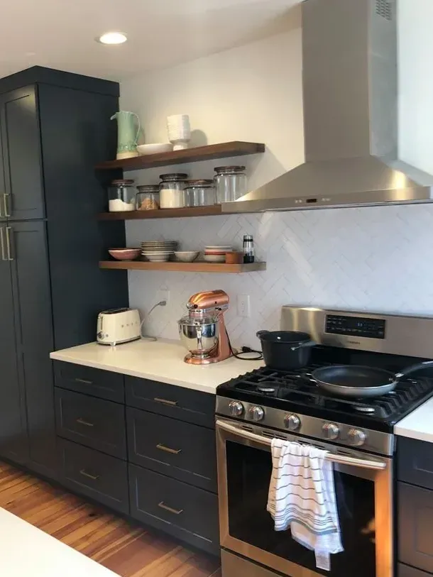 Modern kitchen with dark blue cabinets, stainless steel appliances, and wood shelves against white tiled backsplash.