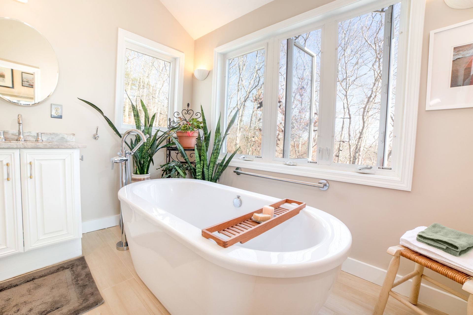A bathroom with a tub, sink, mirror and window.