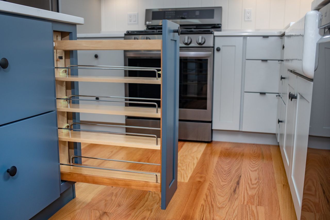 A kitchen with blue cabinets and white cabinets and a pull out spice rack.