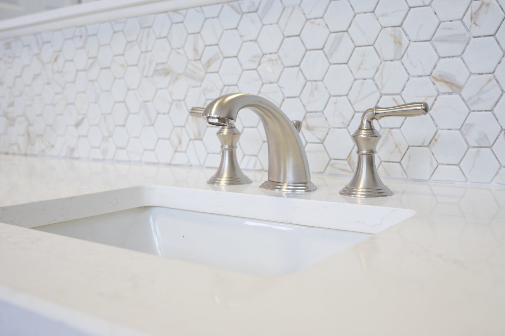 A bathroom sink with a faucet and marble tiles on the wall.
