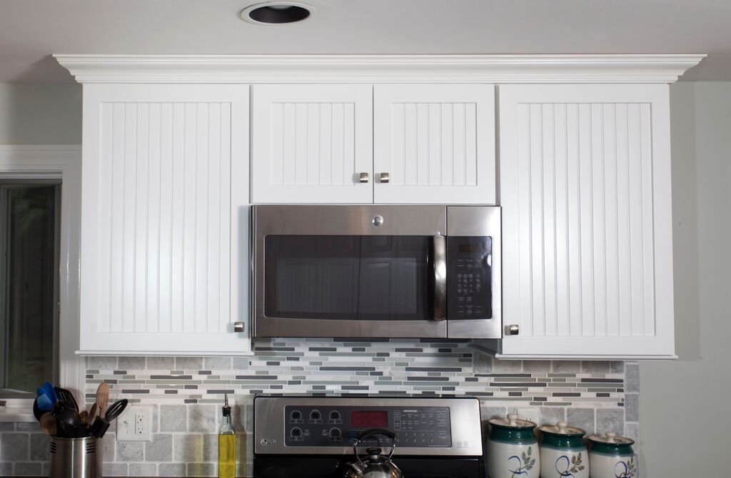 A kitchen with white cabinets , a stove and a microwave.