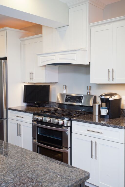 A kitchen with white cabinets , stainless steel appliances and granite counter tops.