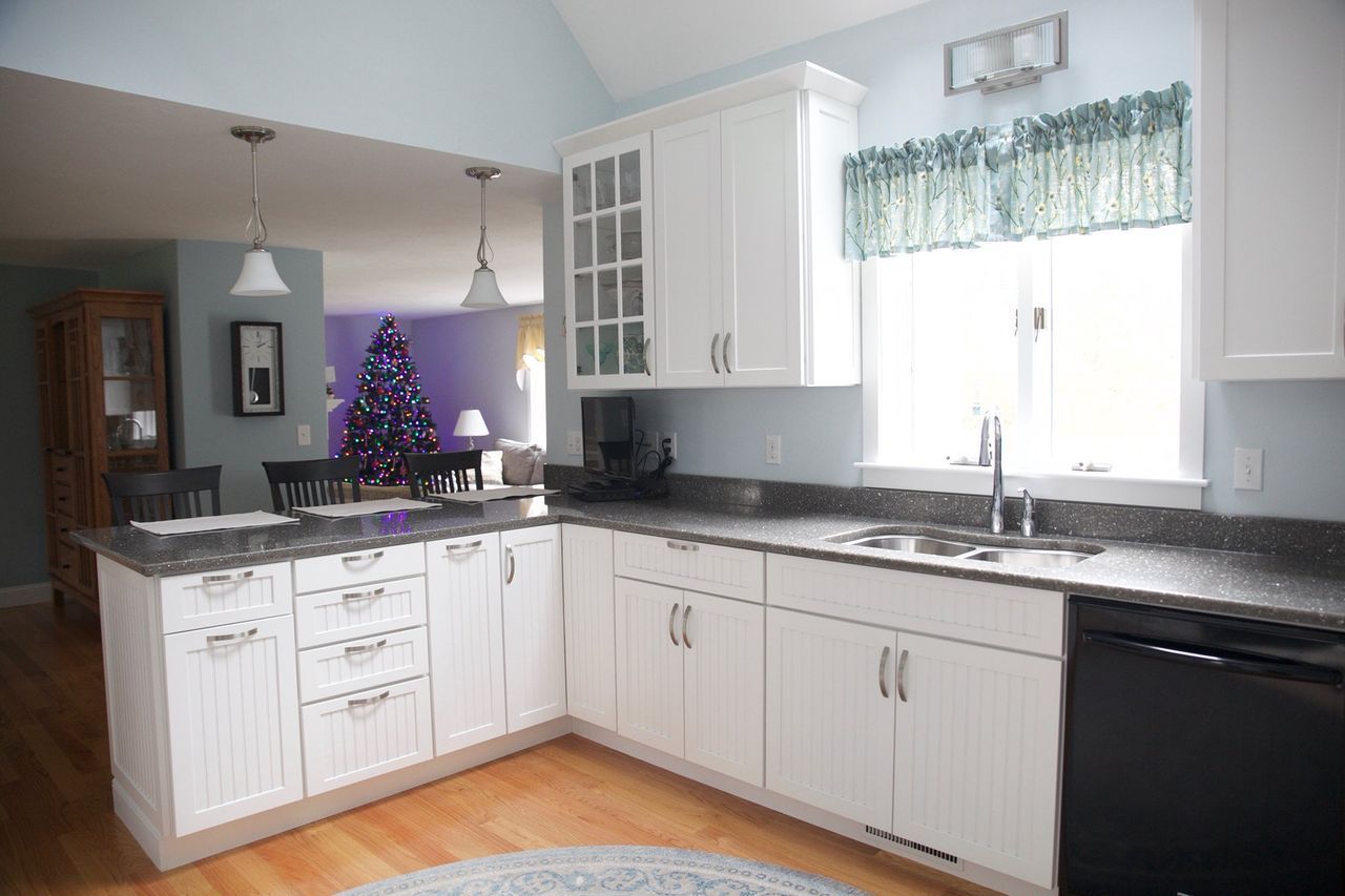 A kitchen with white cabinets and black counter tops and a christmas tree in the background.