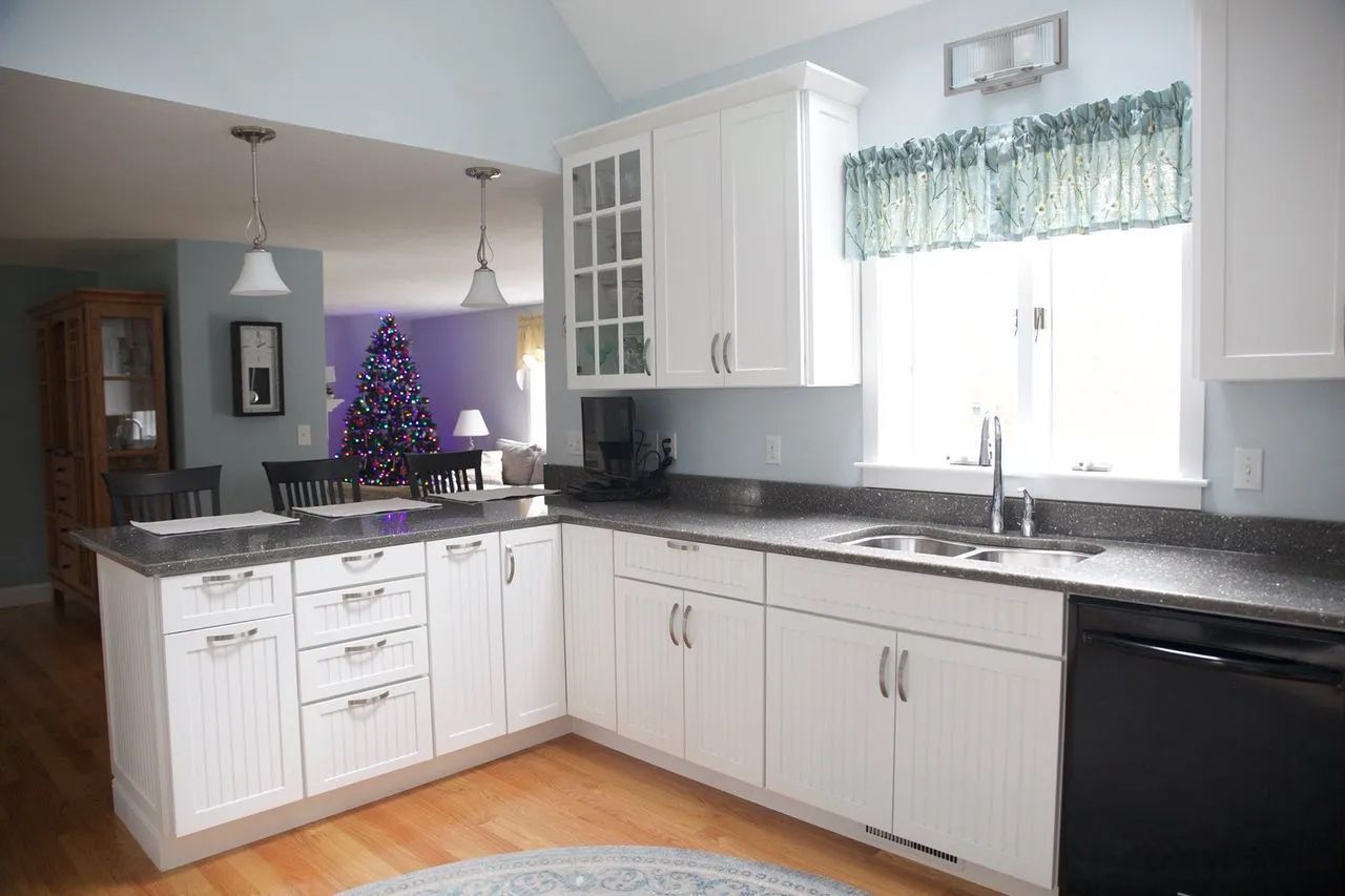 A kitchen with white cabinets and granite counter tops and a christmas tree in the background.