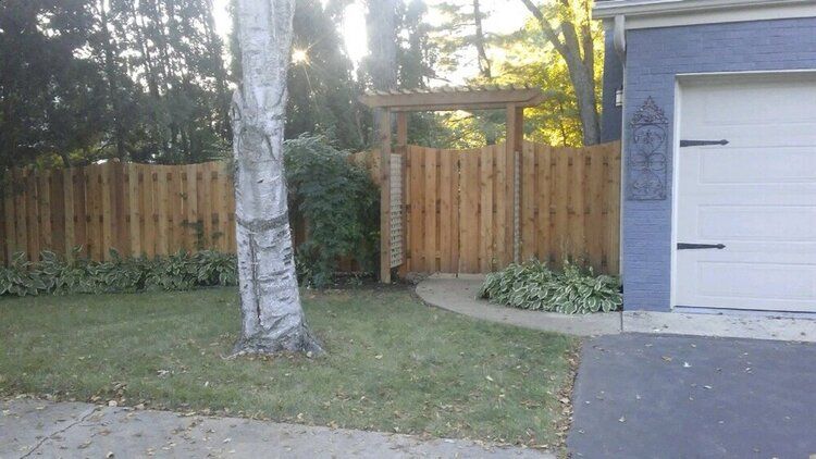 A wooden fence is in front of a blue house with a white garage door.