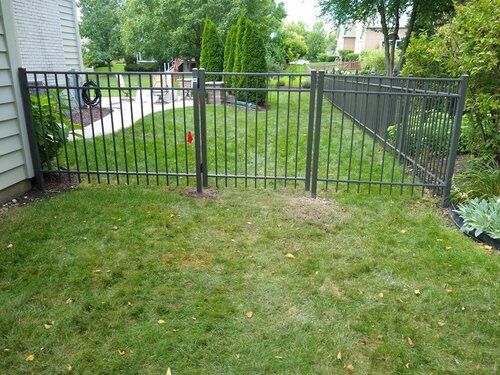 A black metal fence surrounds a lush green yard.