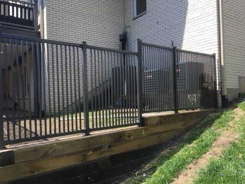 A black fence is surrounding a deck in front of a house.