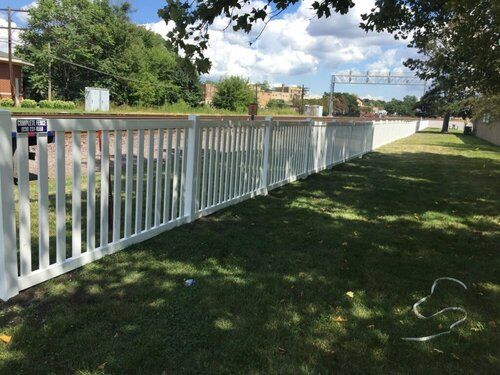 A white fence surrounds a grassy area with a train track in the background.