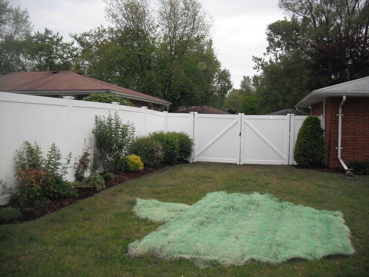 A backyard with a white fence and a green tarp in the grass.