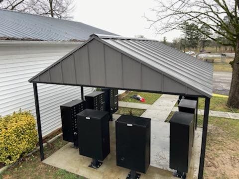 A row of black boxes under a roof in front of a house.