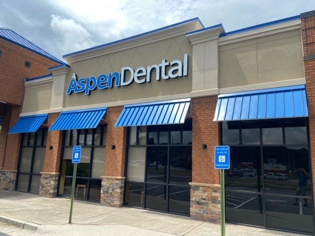 The front of a dental office with blue awnings and a parking sign.