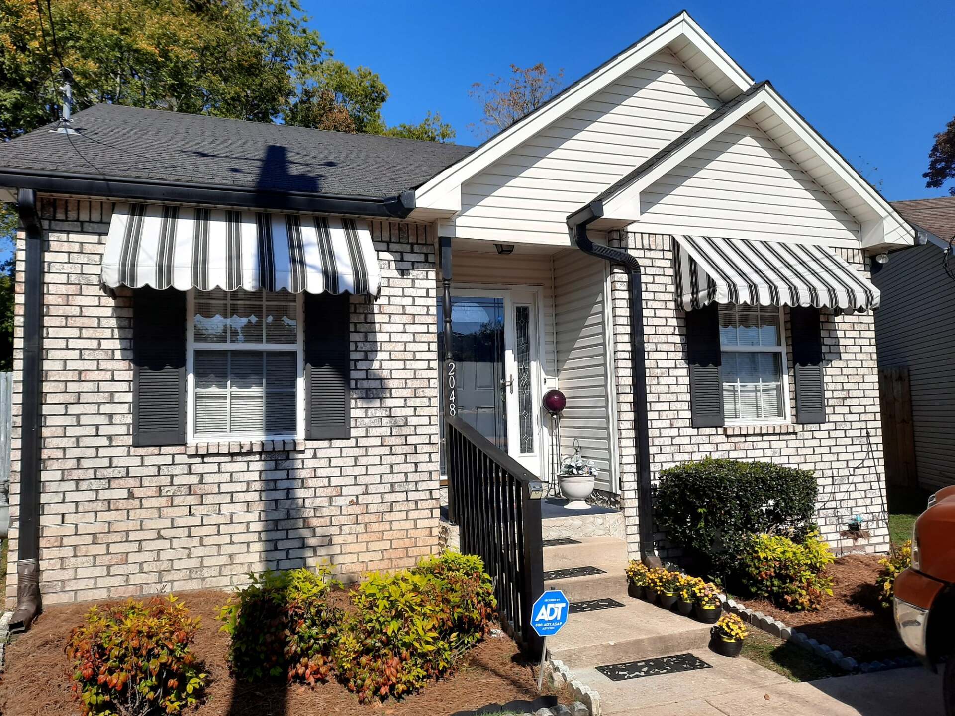 A white brick house with black and white striped awnings on the windows.