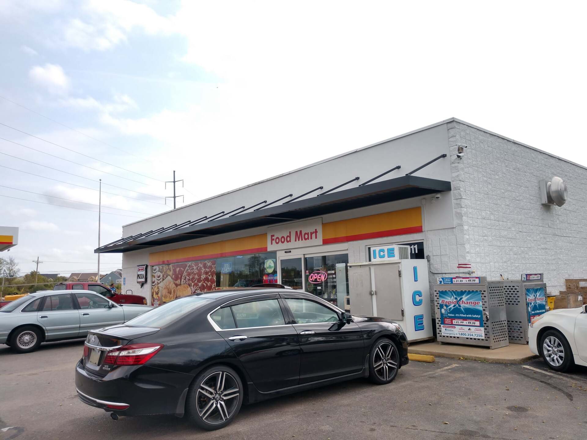 A black car is parked in front of a shell gas station.