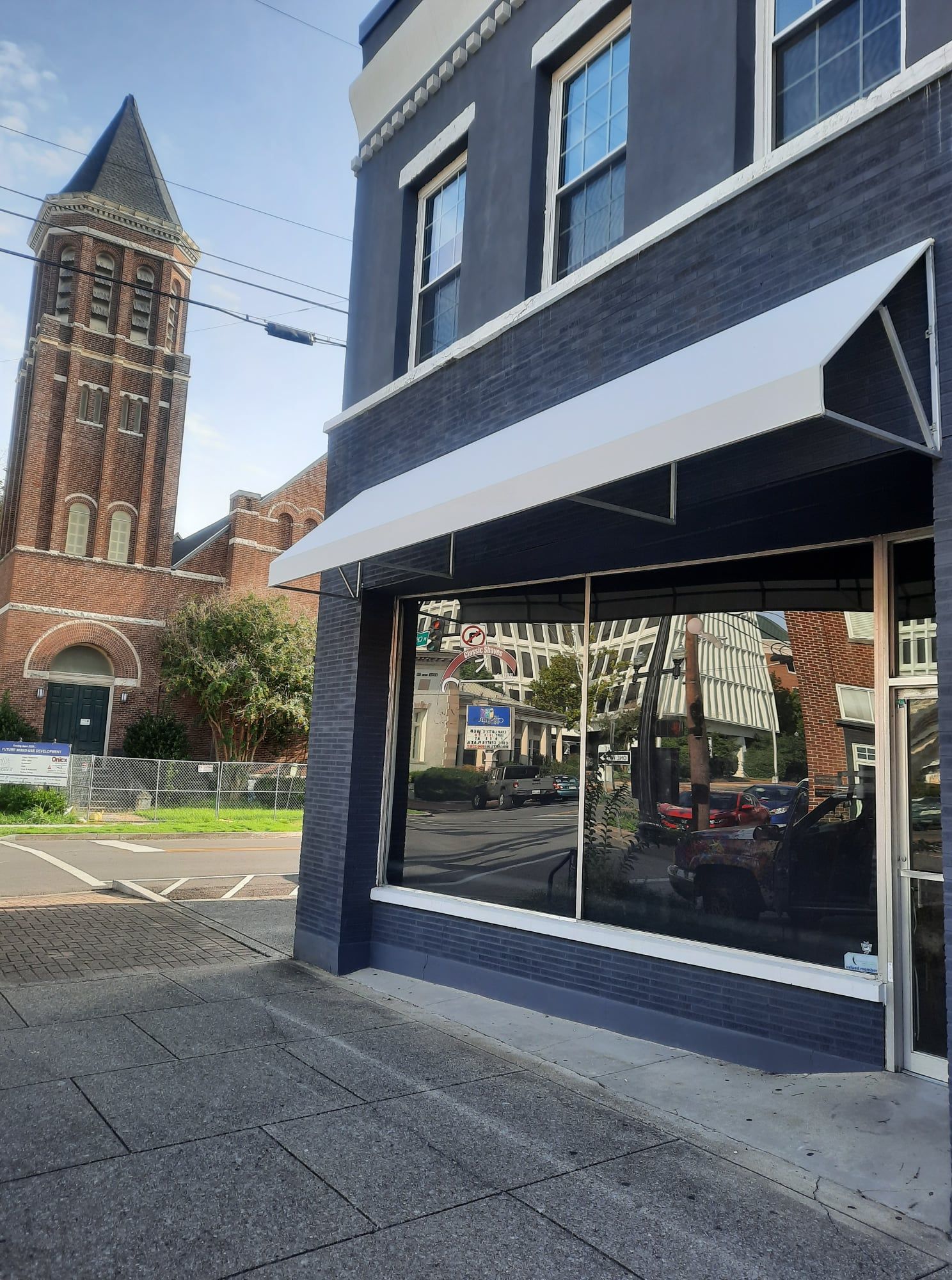 A black building with a white awning and a brick church in the background.